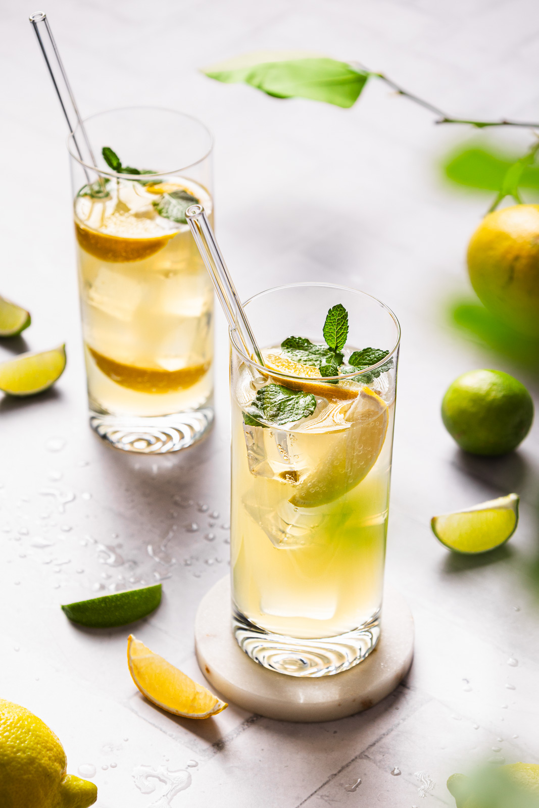 frische Zitronen Limonade in klaren Glaesern mit Eiswuerfeln, Zitronenscheiben, Minze und Glas-Trinkhalmen