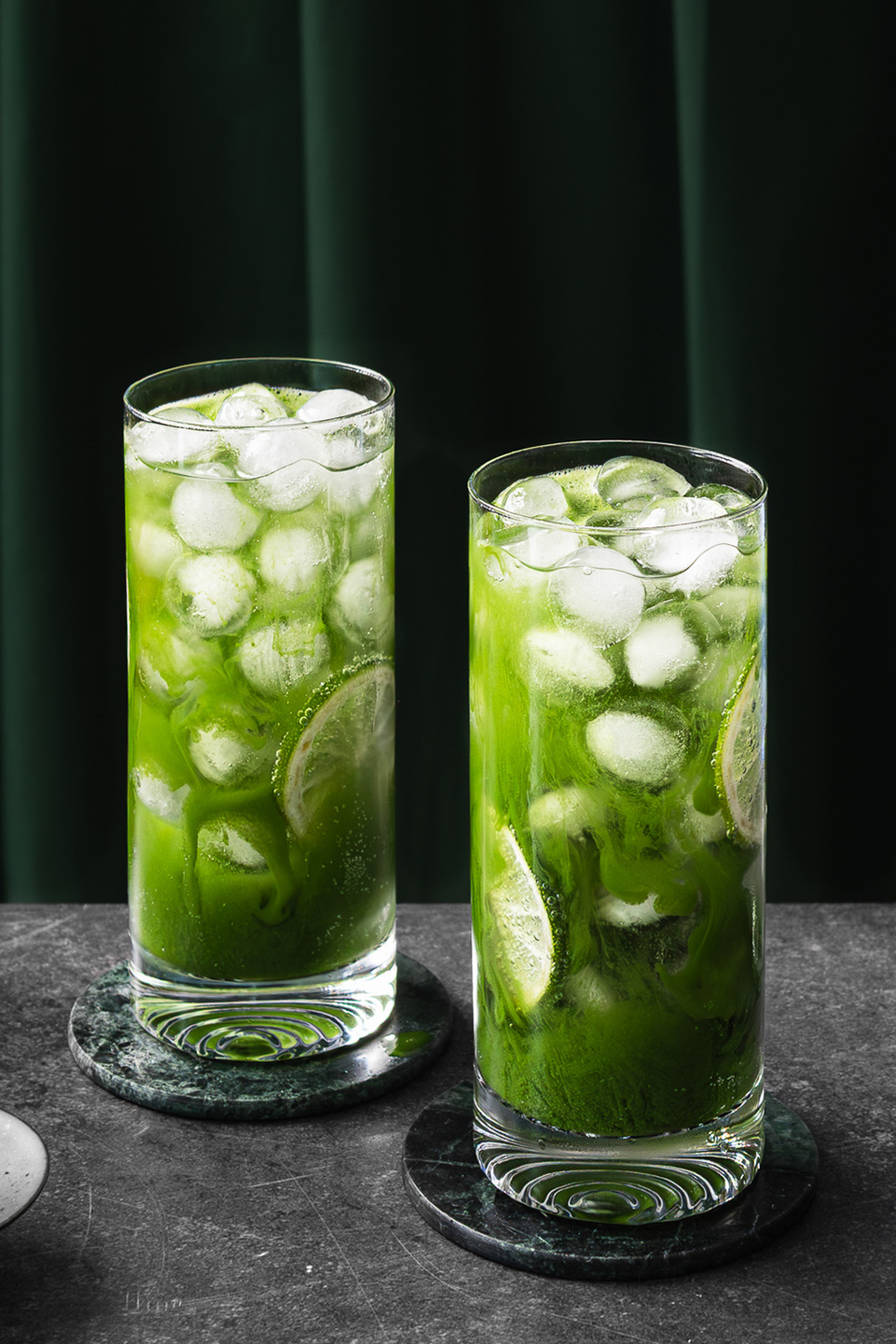 zwei Gläser Matcha Soda mit Eiwürfeln und Limettenscheiben in moderner Getränkefotografie